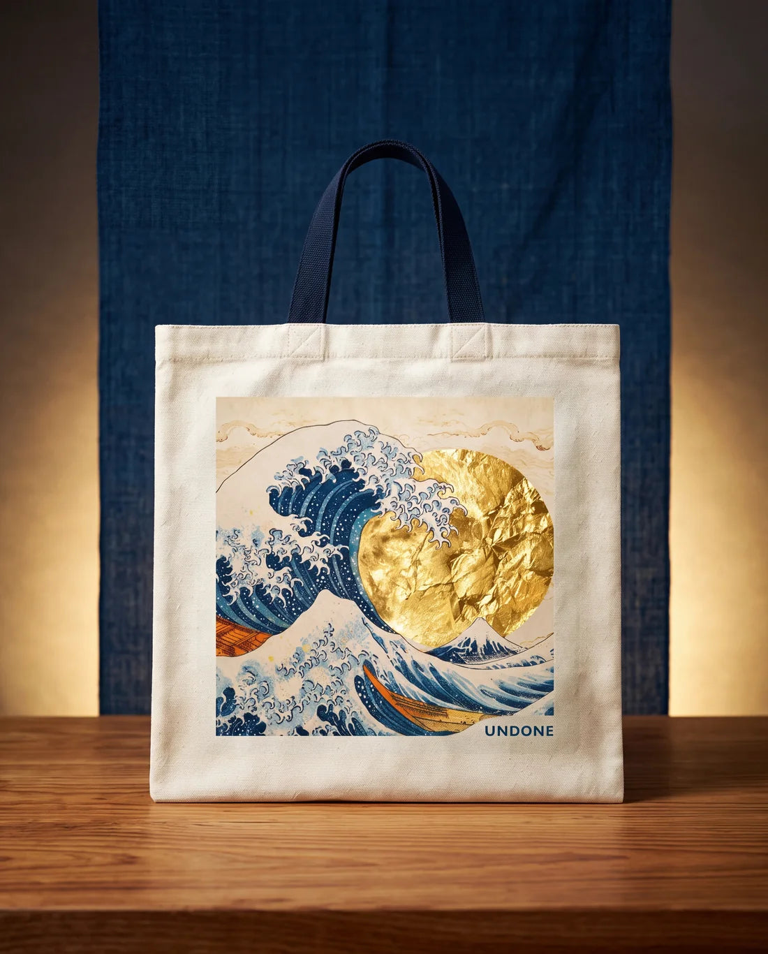 The Hokusai Tote Bag: natural canvas with navy handles, printed with the Great Wave and a gold-leaf sun