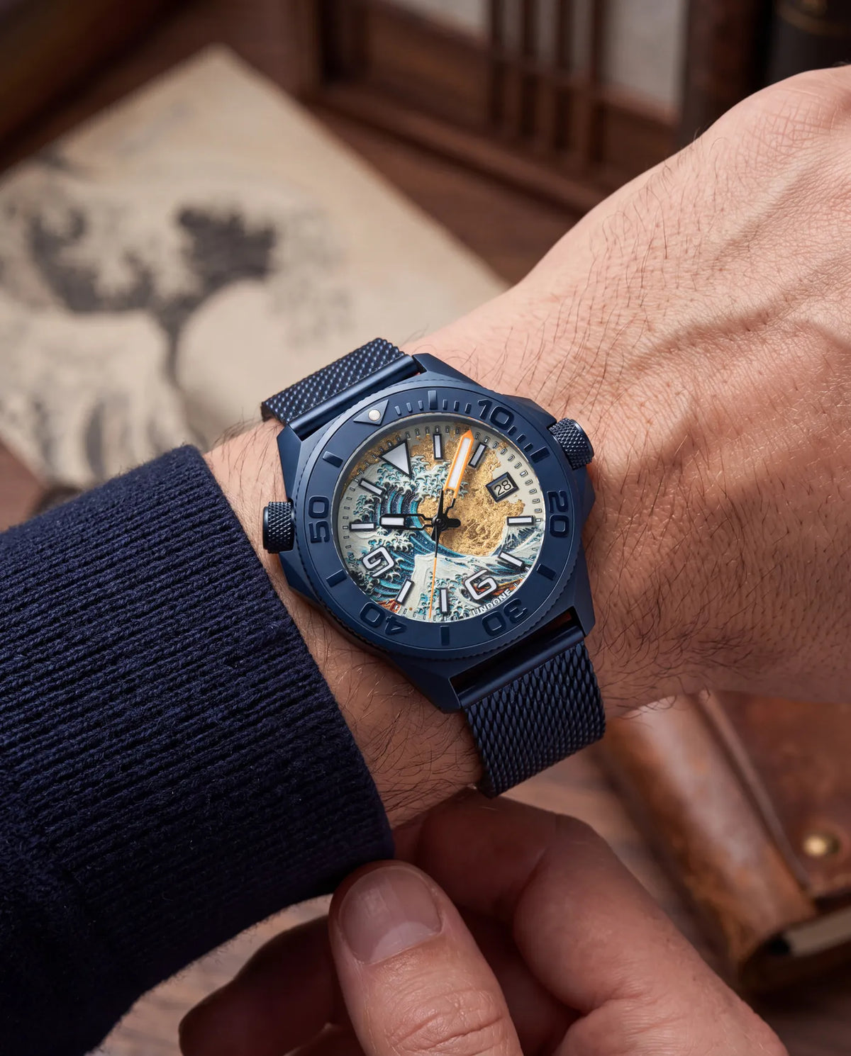 Hokusai II worn on the blue Milanese mesh, a hand settling the strap, a Great Wave print behind