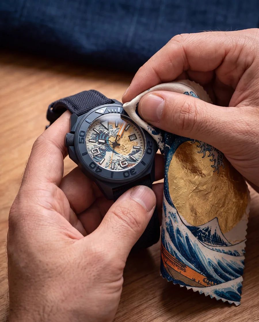 Hands polishing the Hokusai II crystal with the lint-free cloth, printed with the Great Wave and a gold-leaf sun