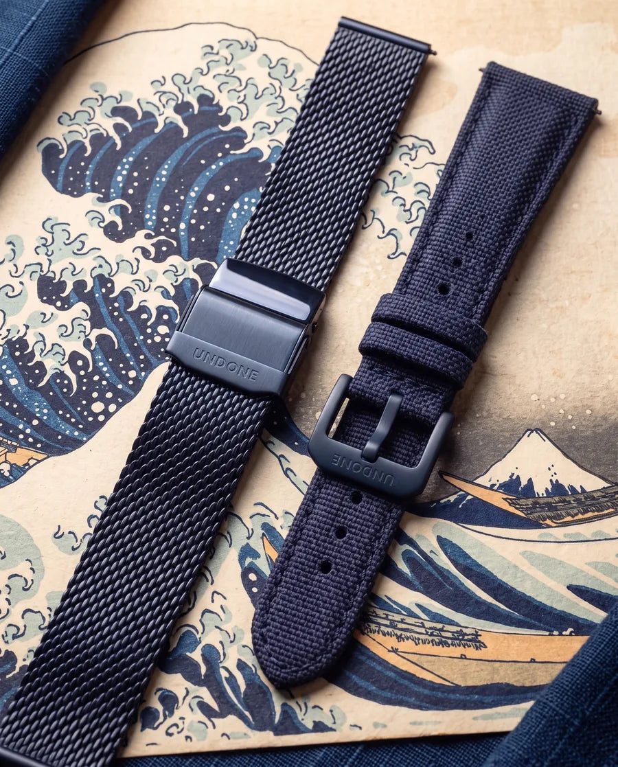 Both straps laid on a Great Wave print: the blue Milanese mesh with its UNDONE deployant clasp, and the navy Cordura with its UNDONE buckle